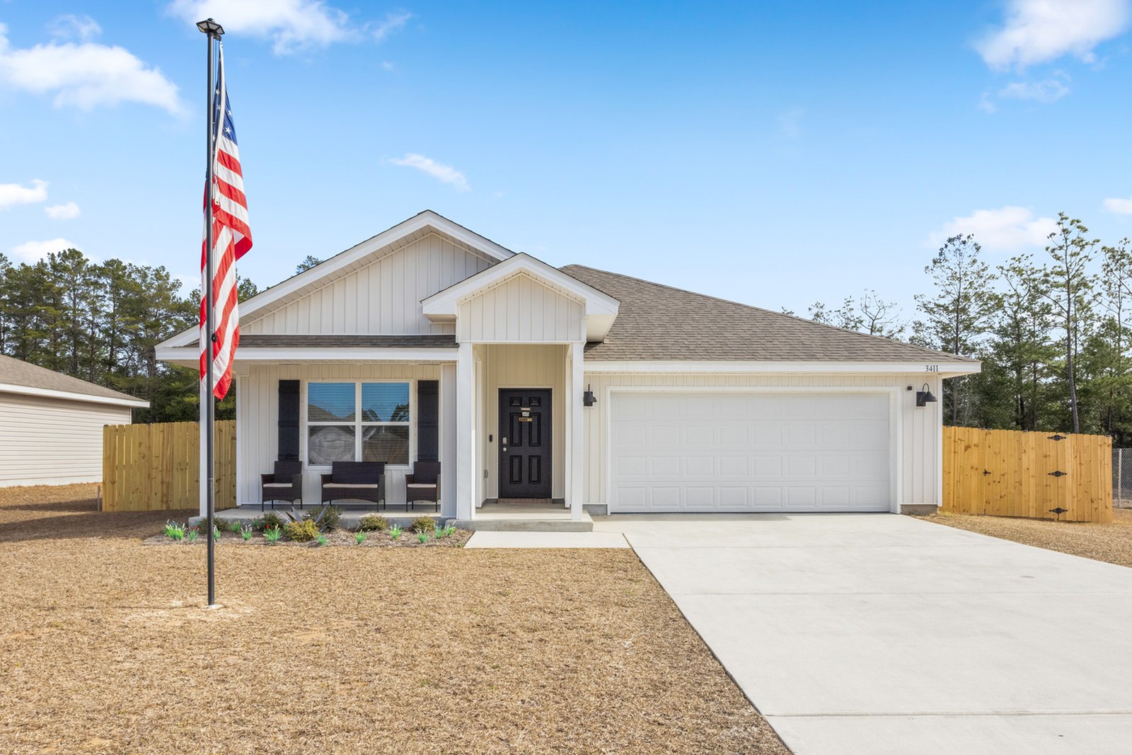 A modern home with American flag and dormant brown front lawn