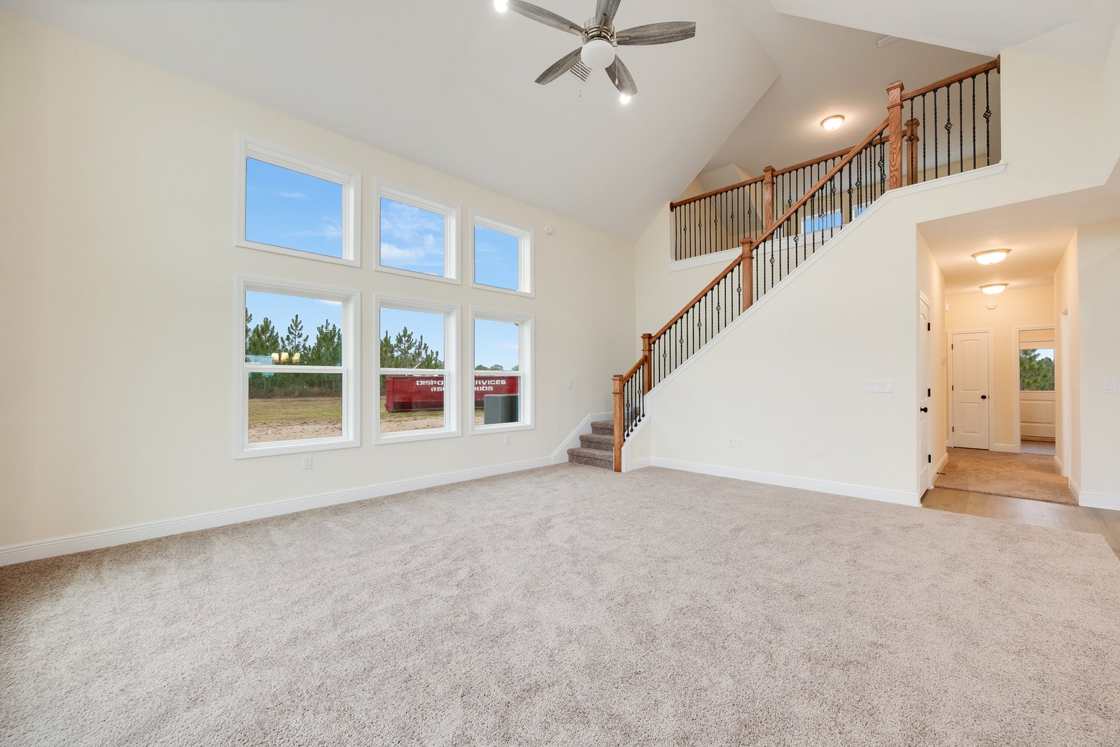 Empty great room with vaulted ceiling, large window bank, and bare carpet