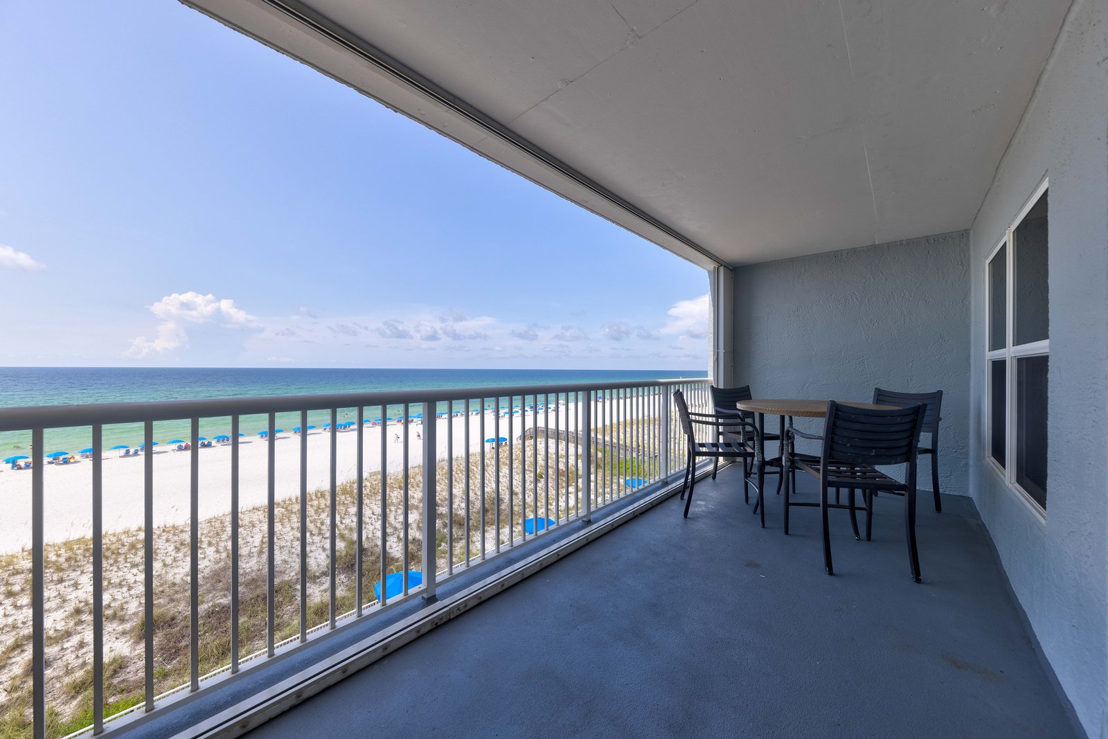Gulf of Mexico view from a beach-front condo balcony with emerald water, white sand, and colorful beach umbrellas